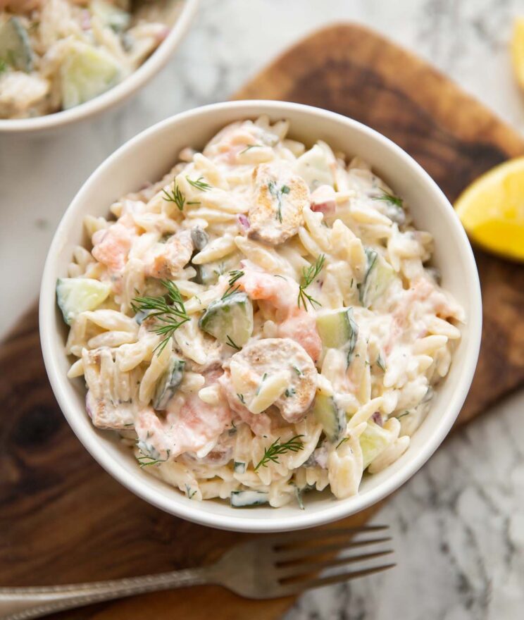 overhead shot of salmon orzo pasta salad in small white bowl on wooden chopping board