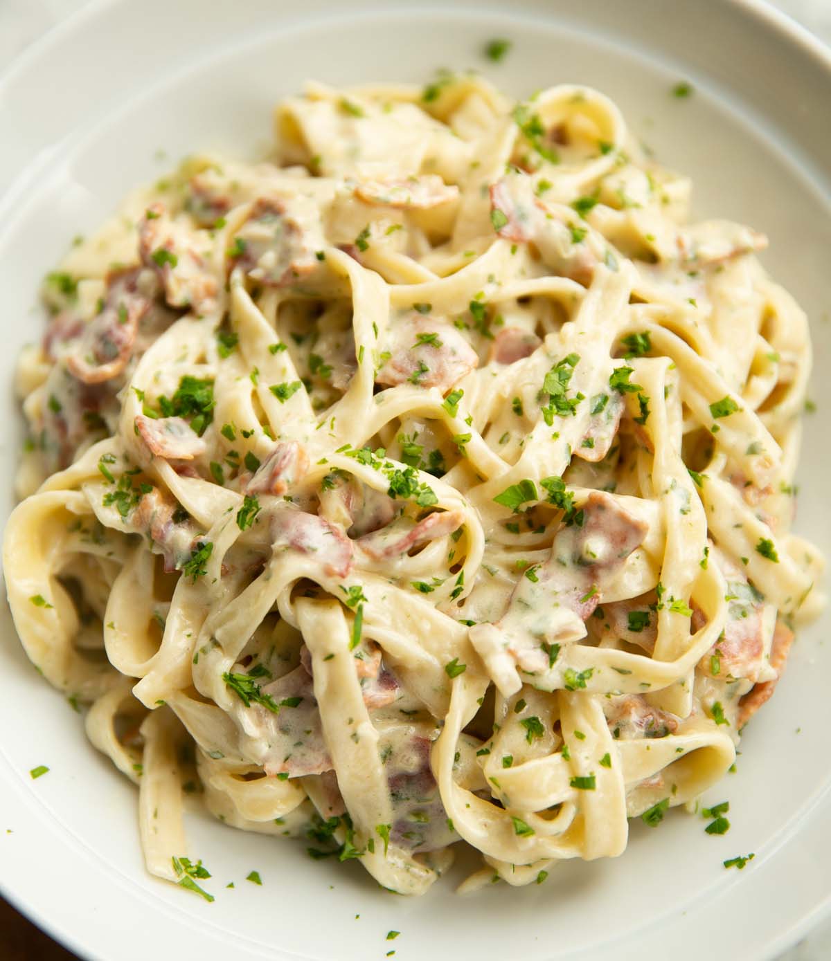 close up shot of creamy bacon pasta in large white dish