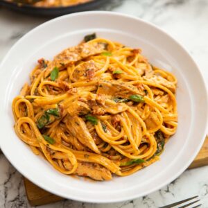 creamy tuscan chicken pasta served in large white bowl on wooden board