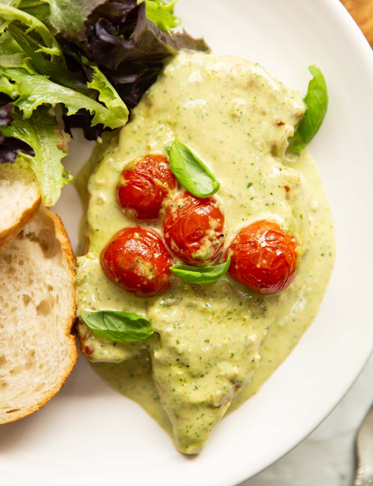 close up overhead shot of creamy pesto chicken on small white plate with bread and salad