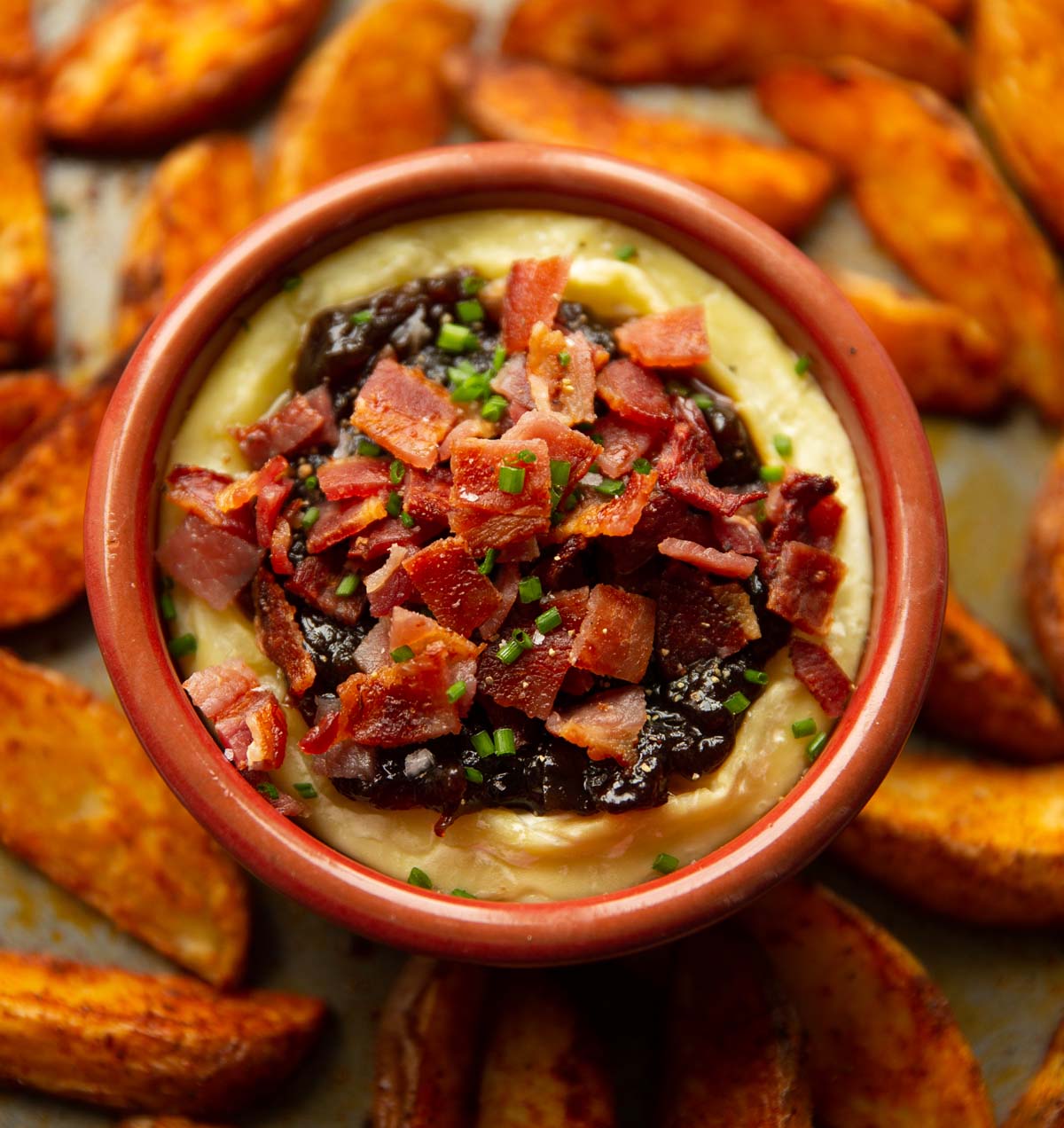 close up shot of bacon baked brie on baking tray surrounded by potato wedges