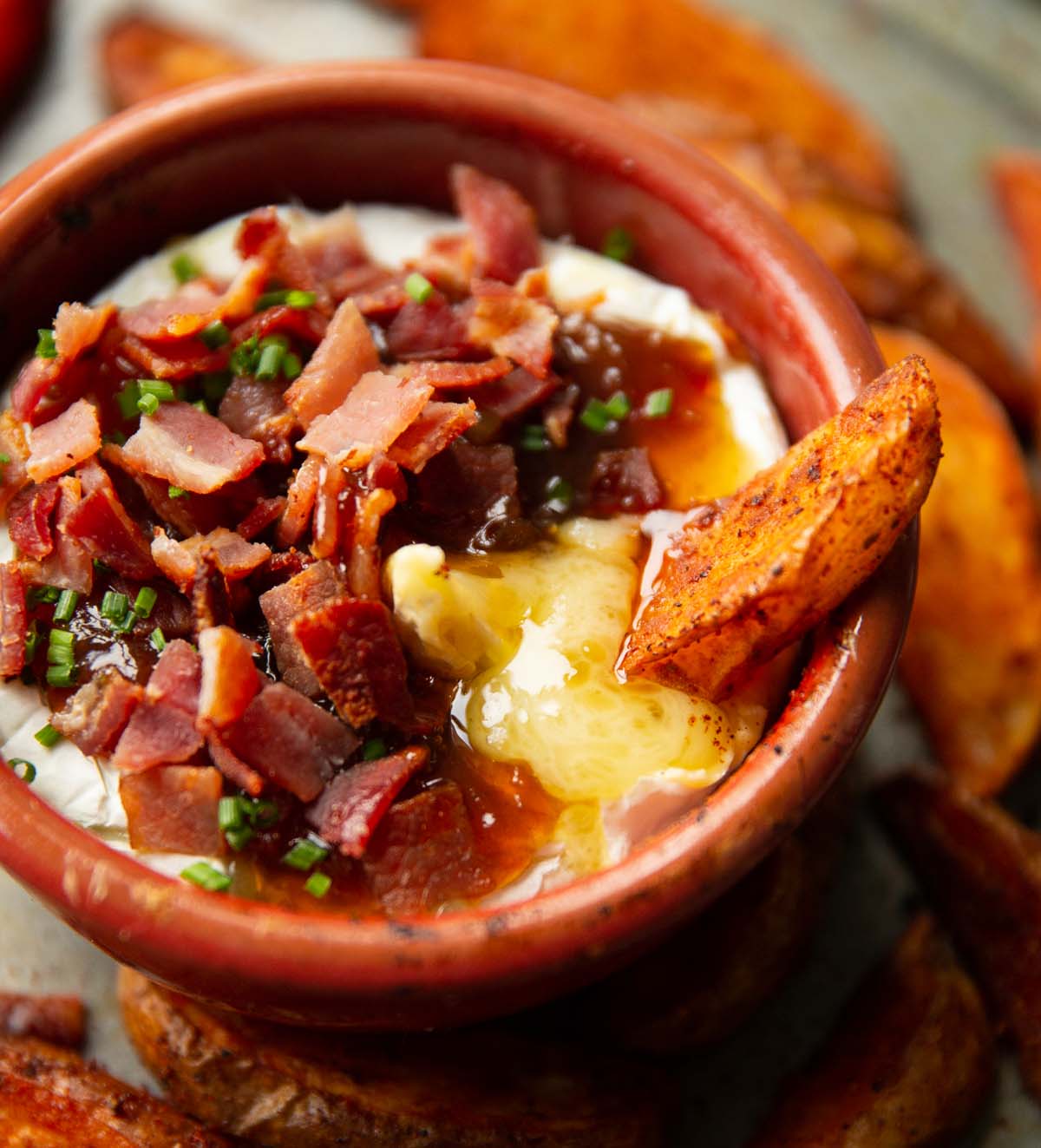 close up shot of potato wedge dunking into baked brie